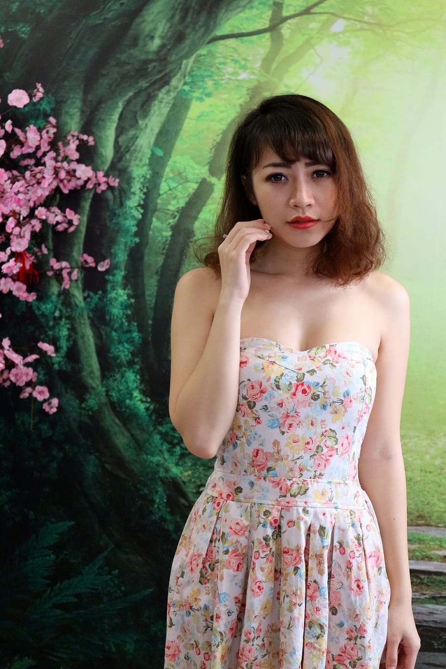 woman wearing white and multicolored floral strapless dress while standing near green tree wall painting