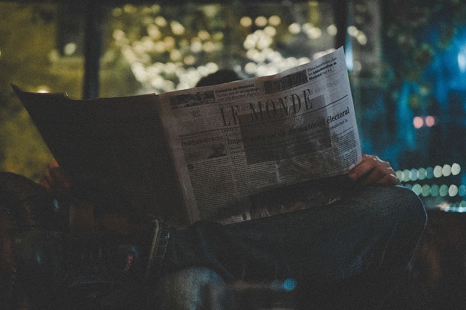 person in jeans reading newspaper, le monde, neon light, bokeh
