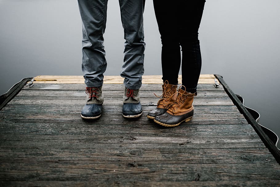 pair of brown boots, two person standing on brown wooden surface while wearing duck boots HD wallpaper
