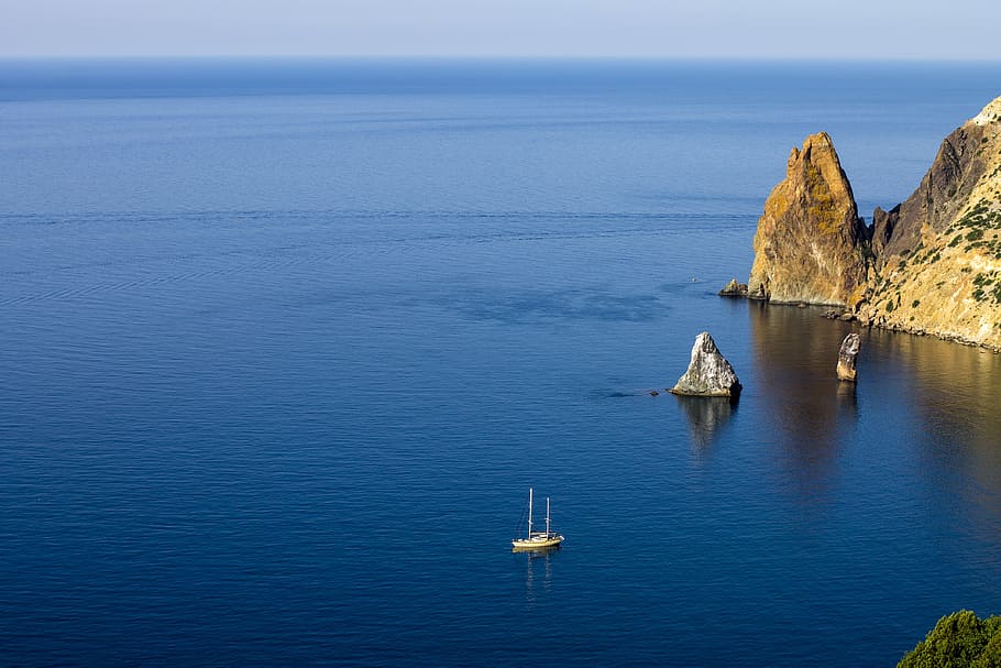 aerial photography of white ship on sea near rock formations under blue sky during daytime, boat on calm sea near rock mountain under blue sky