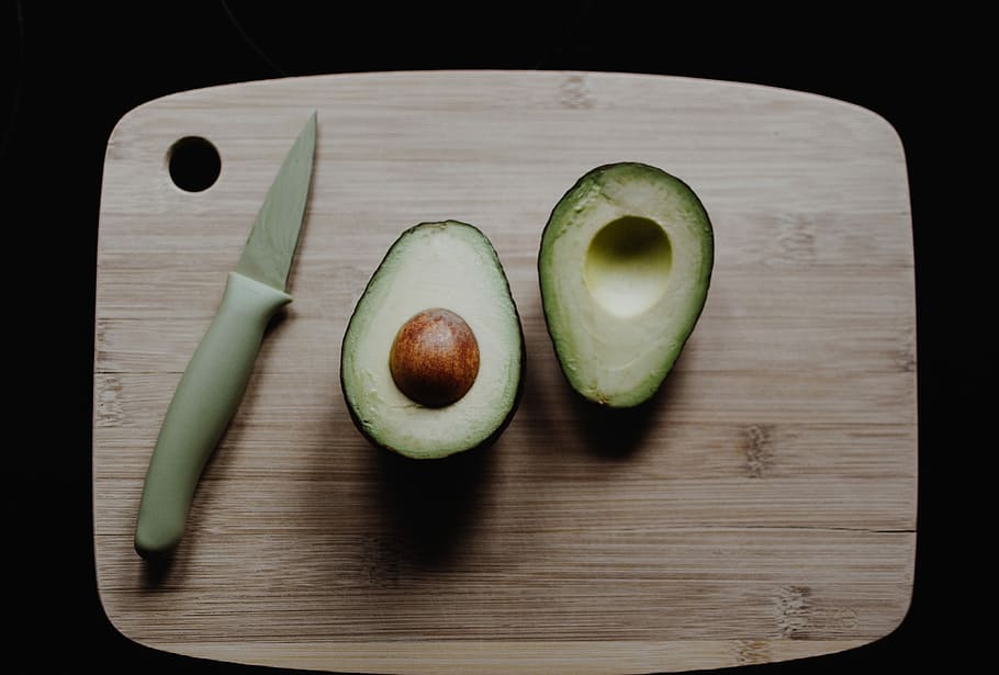 sliced avocados on top of brown wooden chopping board in top view photography, fruit beside knife HD wallpaper