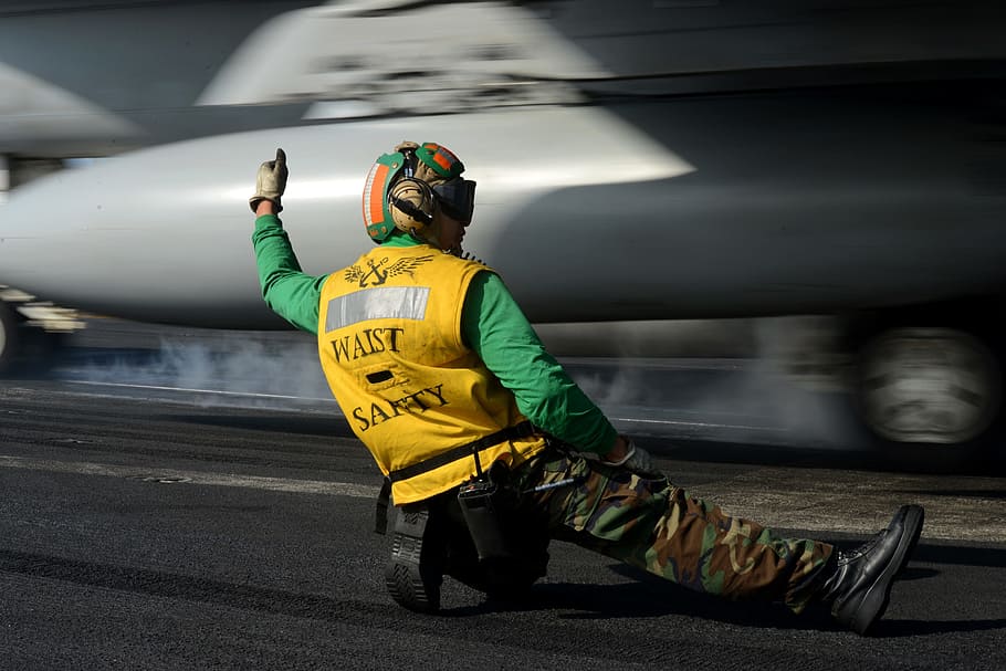 man under gray plane, sailor, signal, launch, jet, aircraft carrier