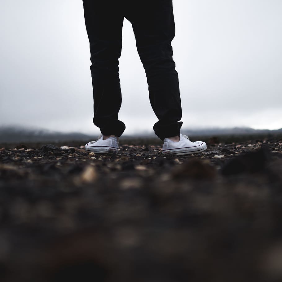 person wearing white low-top sneakers, selective focus photography of man standing on soil