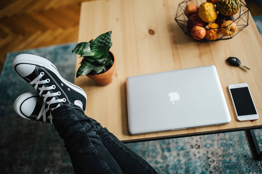 Woman in ripped jeans and black sneakers with a silver laptop on a wooden table HD wallpaper