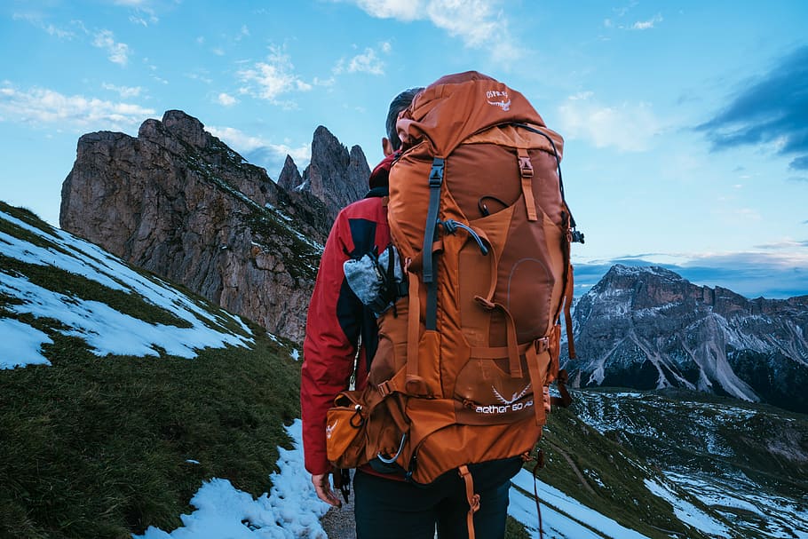man carrying backpack standing on mountain during daytime, photo of person carrying orange hiking backpack HD wallpaper
