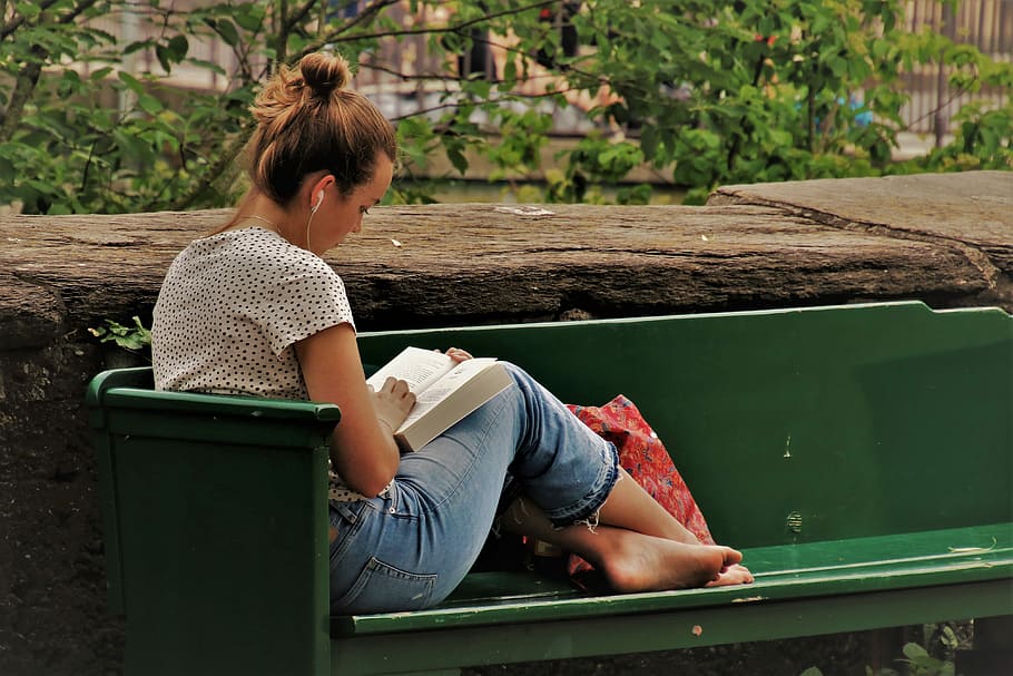 woman in blue denim pants reading book on green bench during daytime HD wallpaper