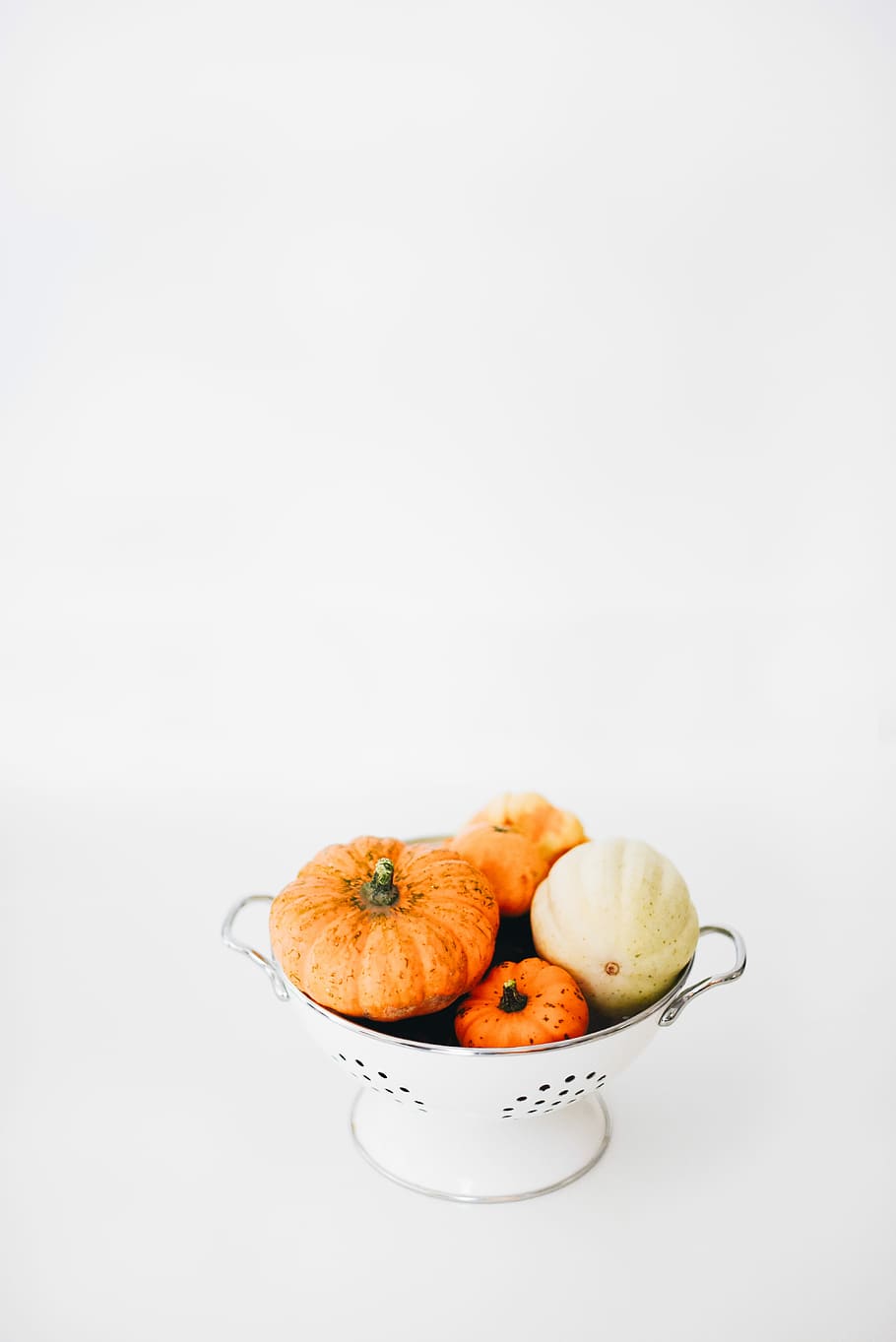 four round orange squashes on colander, assorted vegetables on stainless steel strainer