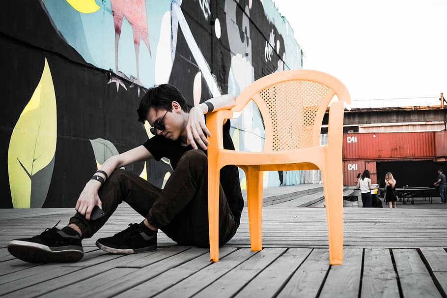 man sitting on floor beside empty orange plastic monobloc armchair at daytime, man sitting beside orange plastic armchair HD wallpaper