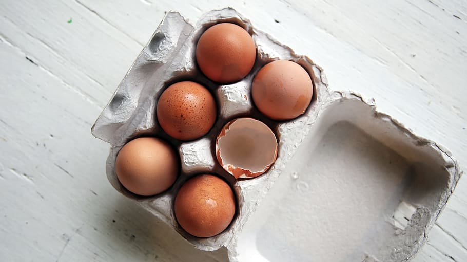 five whole eggs and one empty half-open egg inside open egg tray, photo of six brown eggs on grey tray