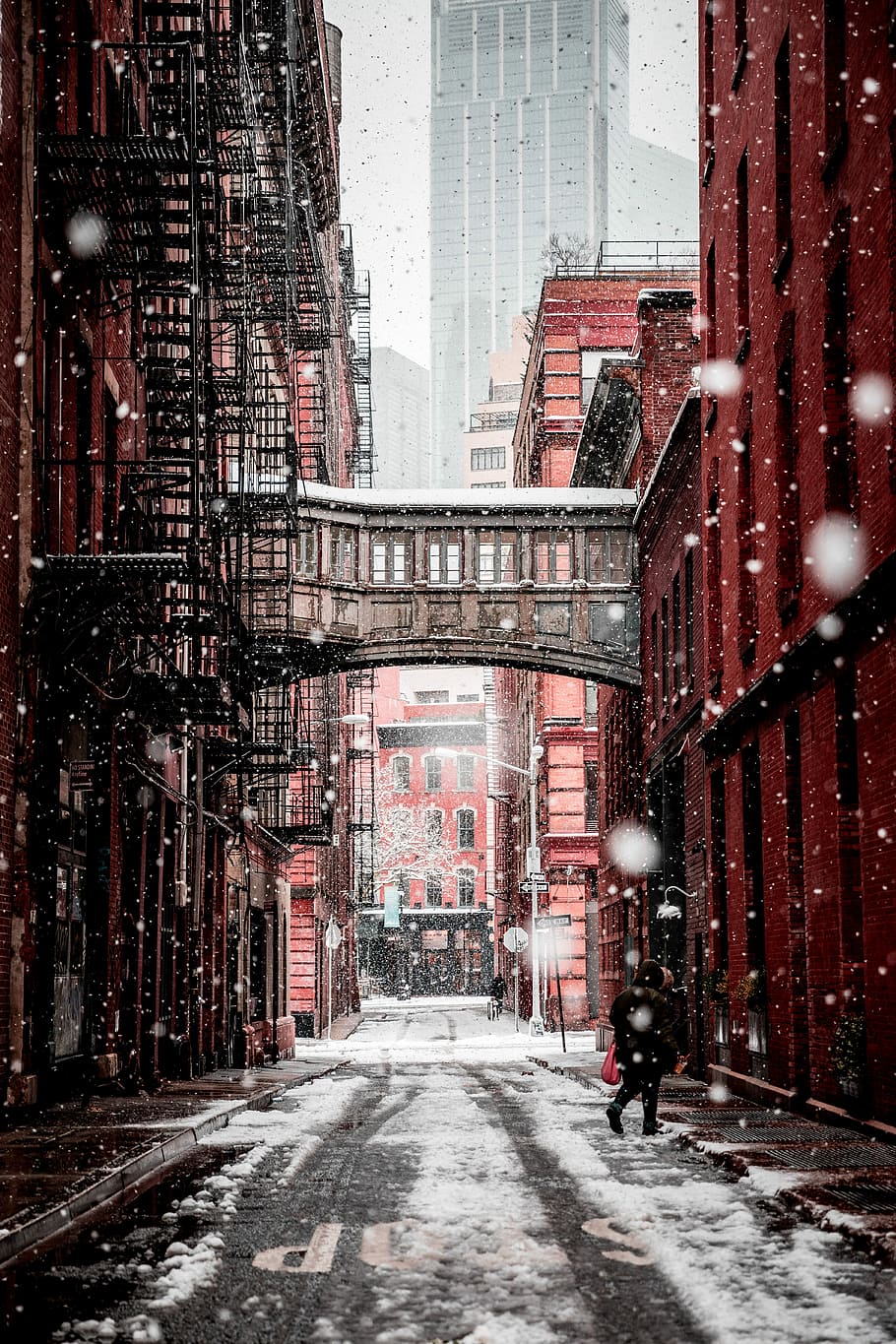 person walking on the street during daytime, pathway between buildings during snow time