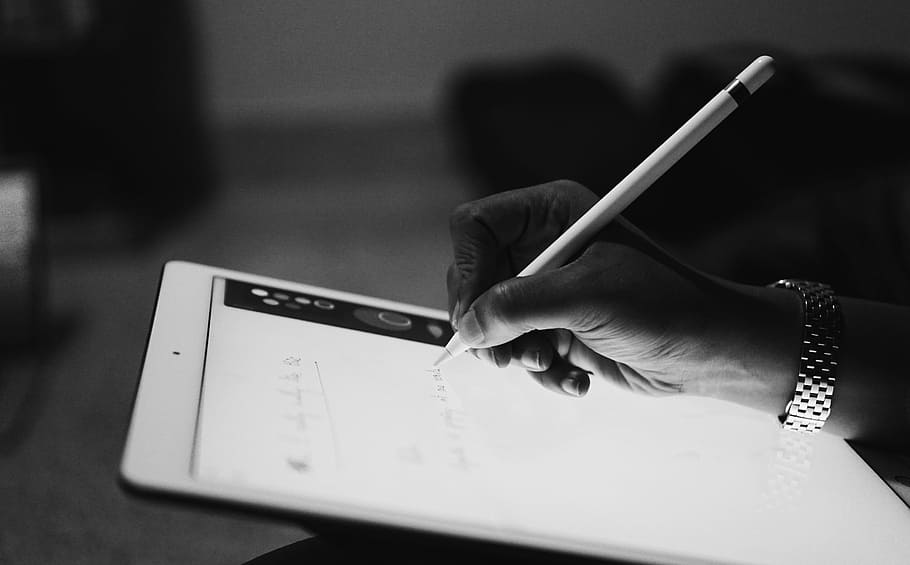 person typing by Apple Pencil on iPad in a room, grayscale photo of person drawing on tablet computer