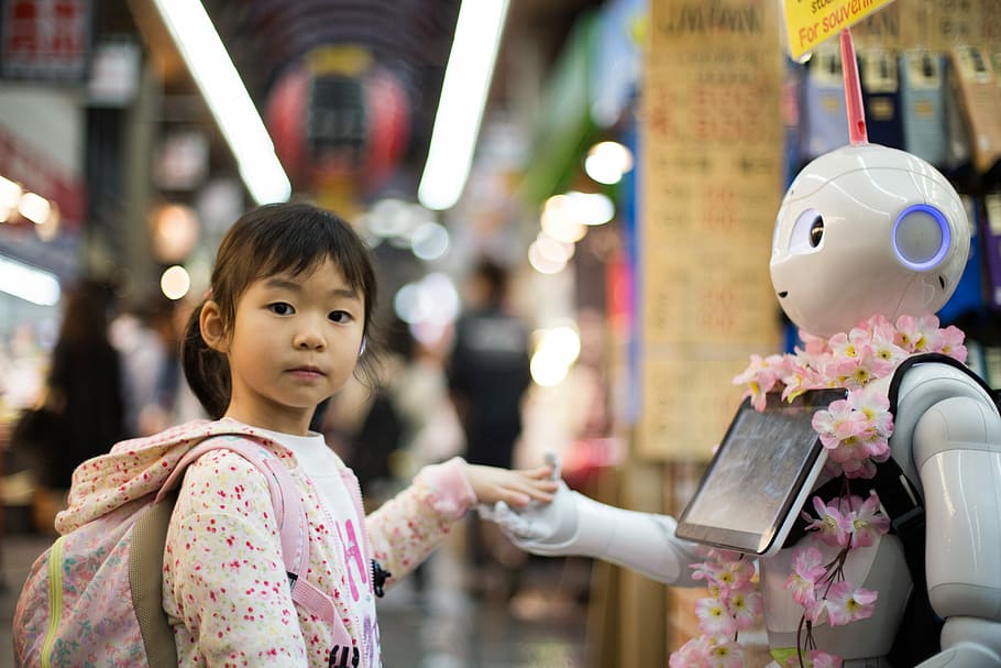 photo of girl laying left hand on white digital robot, girl holding hand of automated robot