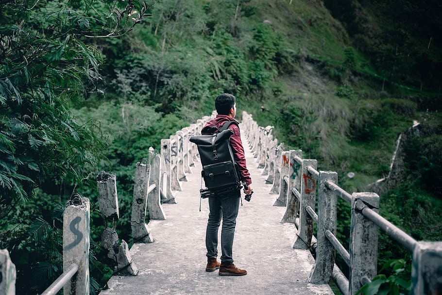 man standing on gray concrete bridge taken at daytime, man standing on footbridge in the middle of rainforest HD wallpaper