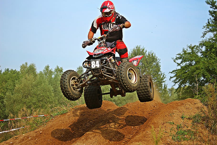 man driving red and black ATV jumps in hill, quad, cross, enduro