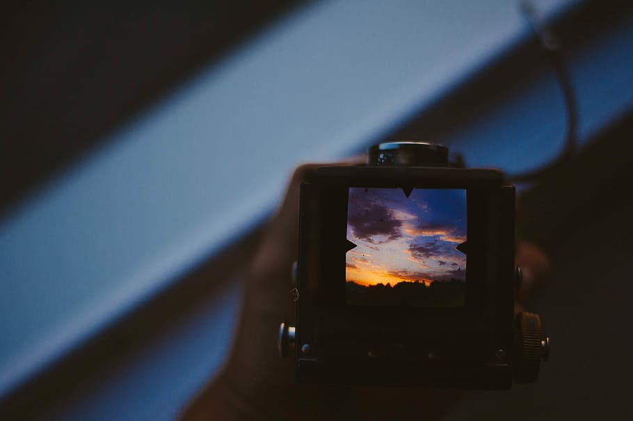 person holding camera, person holding black camera, sky, sunset
