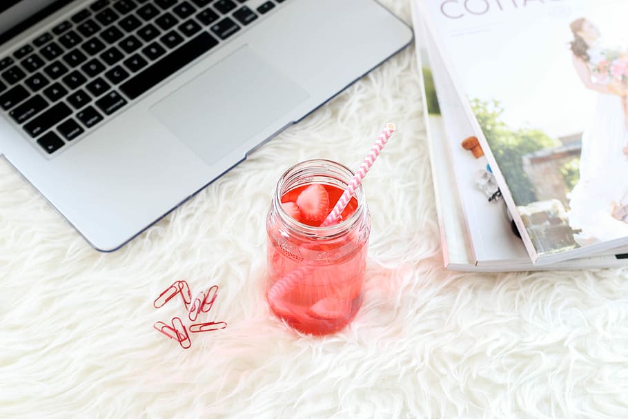 clear mason jar with red liquid and straw, flat-lay photography of pink liquid drink near silver MacBook HD wallpaper