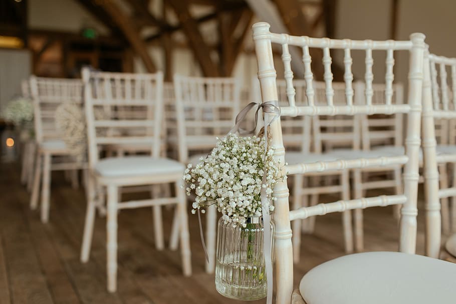 white petaled flowers on jar hang in chair, white chairs with white flowers on clear glass vase