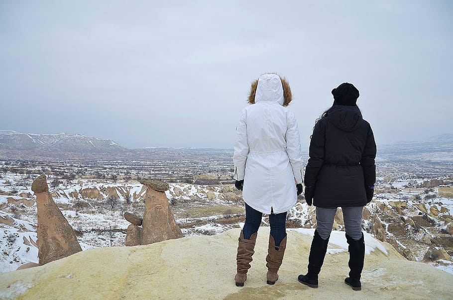 two person wearing black and white hooded jacket standing on rock formation during daytime