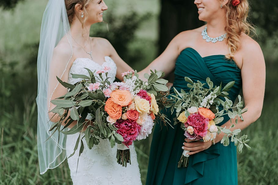 bride holding bouquet of assorted-color flowers standing on grass field, bride near woman in green gown