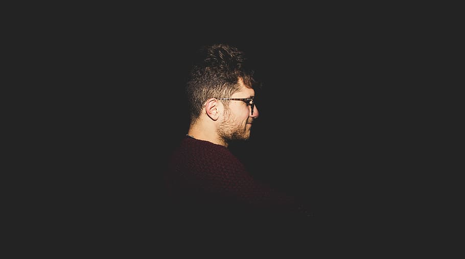 man facing right inside dark room, bearded man wearing glasses HD wallpaper