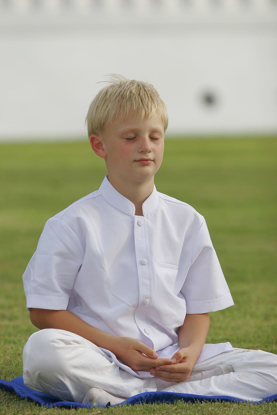 boy wearing white outfit while meditating on green grass field HD wallpaper