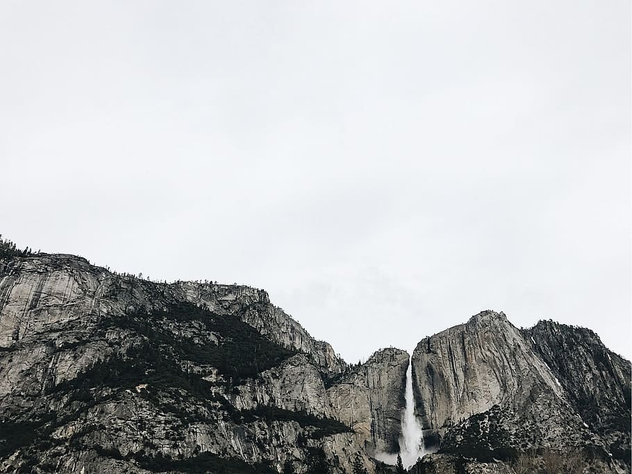 waterfalls under white sky, low angle photography of rocky mountain under white cloudy skies HD wallpaper