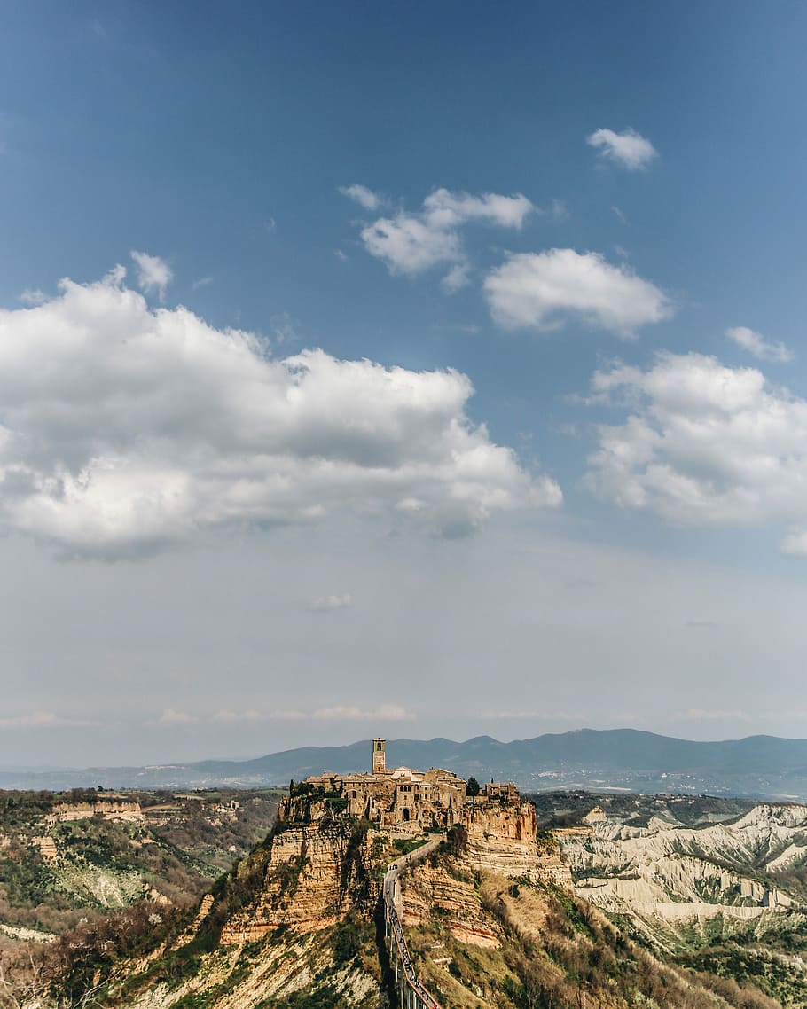 brown rock formation under white and blue sky, brown establishment on the top of the mountain during daytime HD wallpaper
