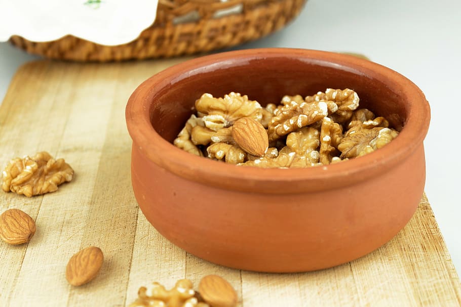 photo of brown almond brittles in brown clay pot, walnut, dried fruits and nuts