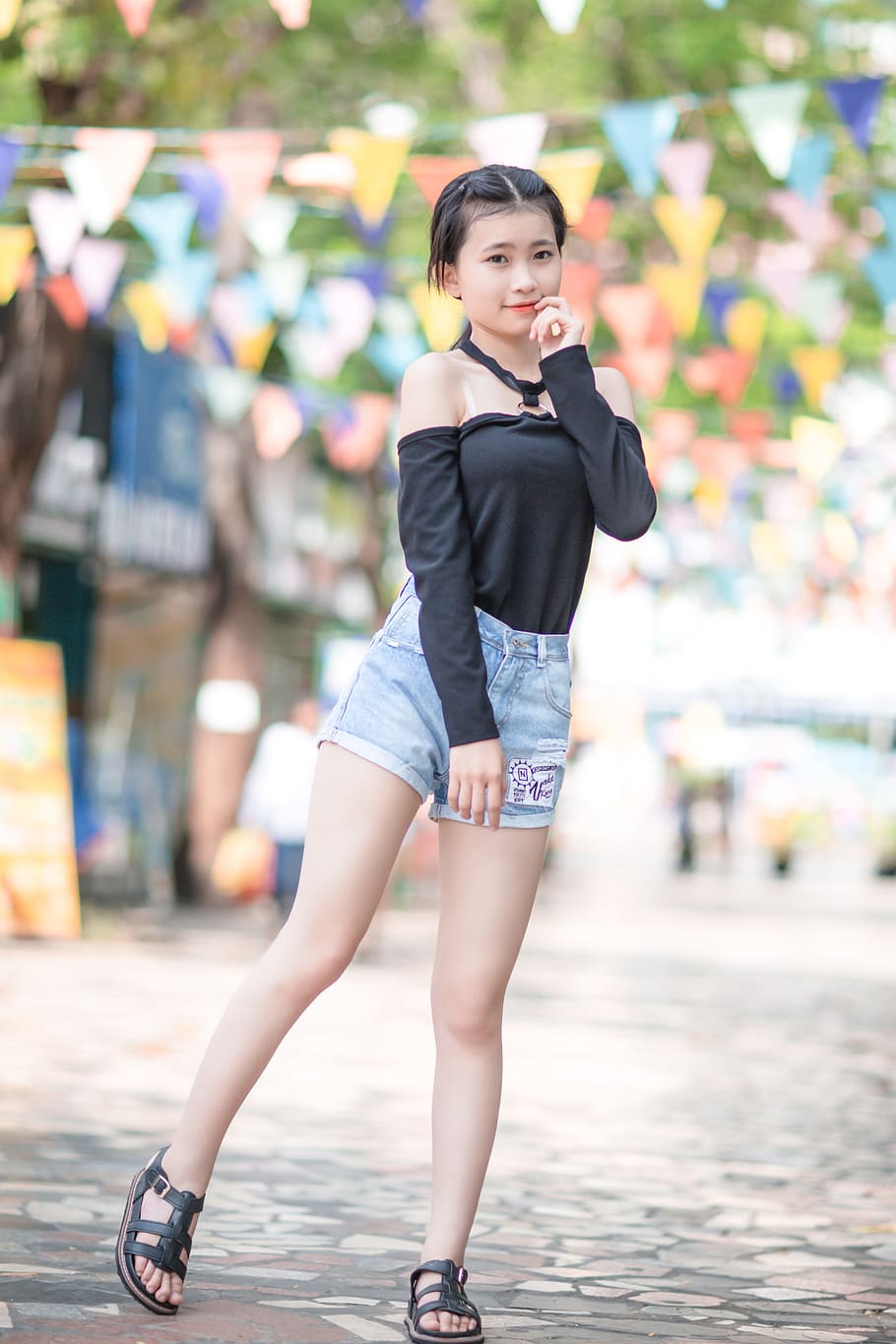 girl in black cold-shoulder blouse and blue stone-washed denim cuffed short shorts outfit having pictorial during daytime