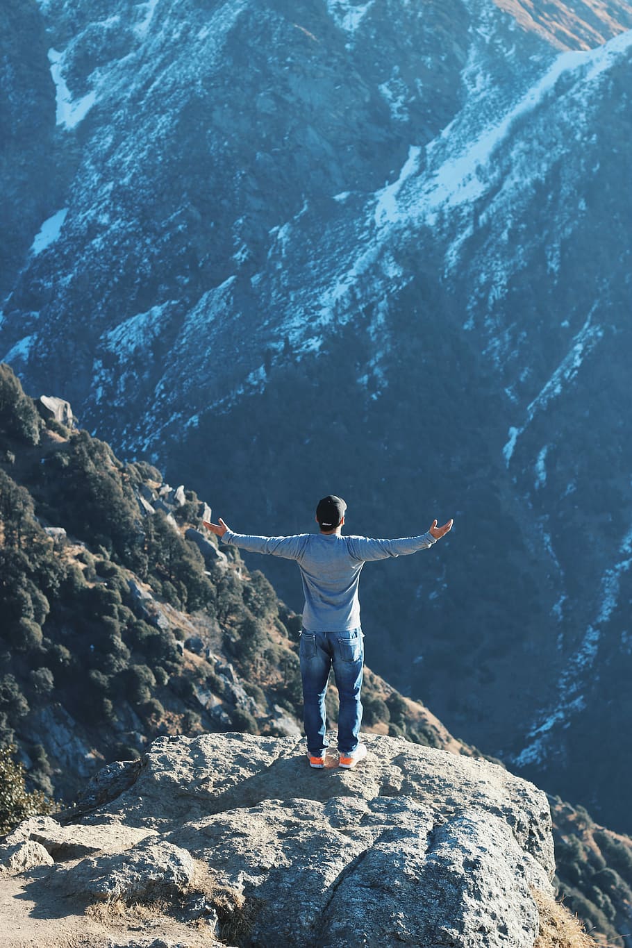 person standing on rock mountain while raising his hand sideways, man spreading his arms on top of mountain