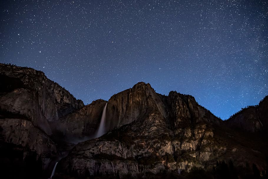 waterfalls on rock cliff, shallow photography of mountain under night sky HD wallpaper
