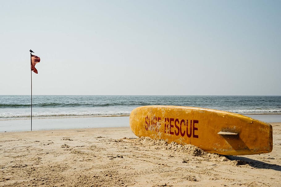 brown surf rescue surfboard near flag pole, india, goa, beach