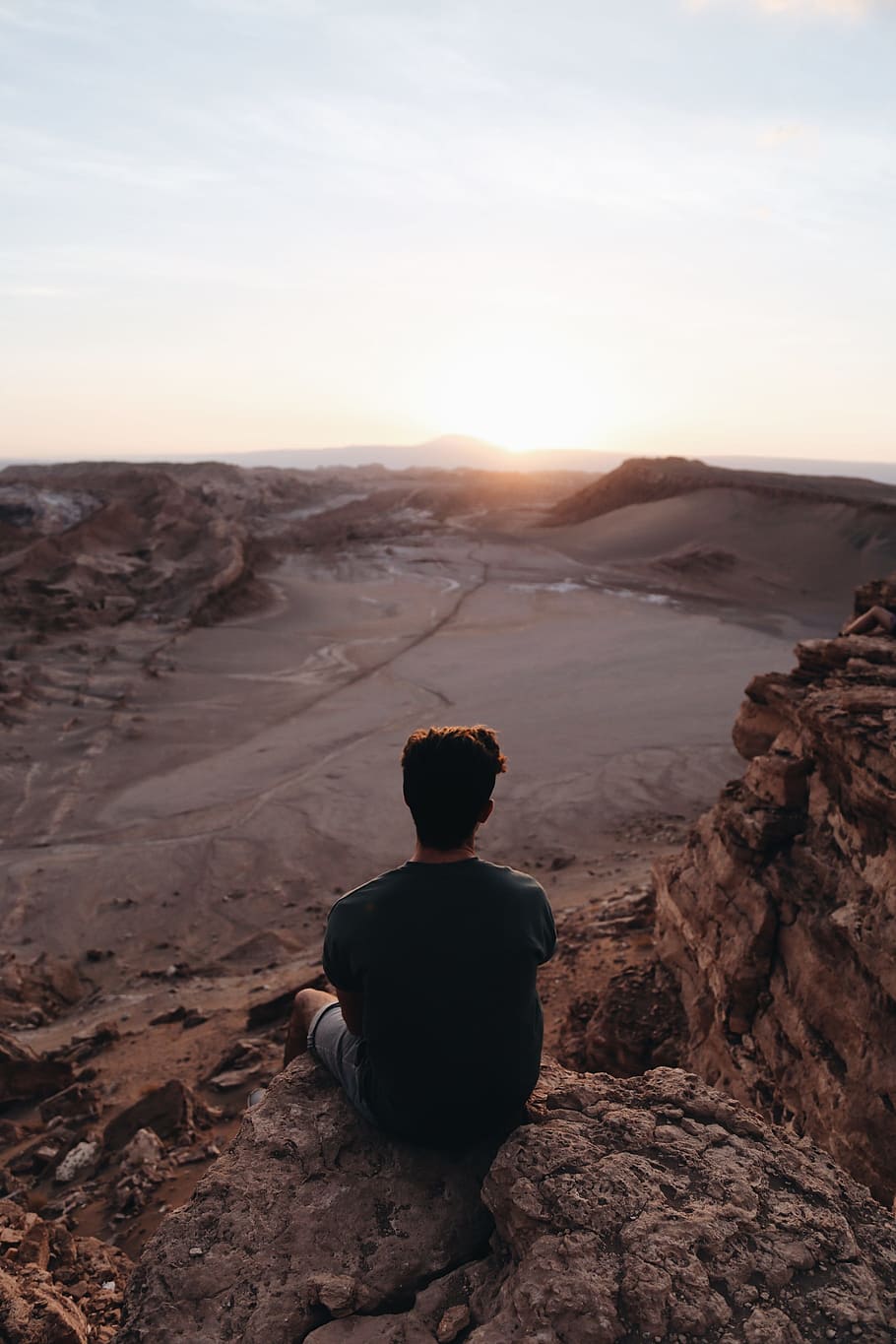 man sitting on cliff facing open field during daytime, person sitting on rock cliff during daytime HD wallpaper