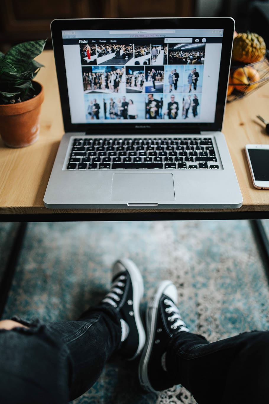 Woman in ripped jeans and black sneakers with a silver laptop on a wooden table HD wallpaper
