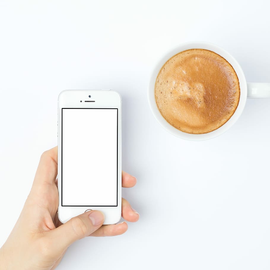 person silver iPhone 5s beside white ceramic mug, person holding silver iPhone 5s near white ceramic coffee cup with coffee HD wallpaper