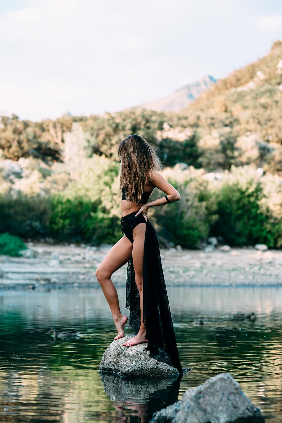 woman wearing black crop top standing at gray stone on body of water during daytime HD wallpaper