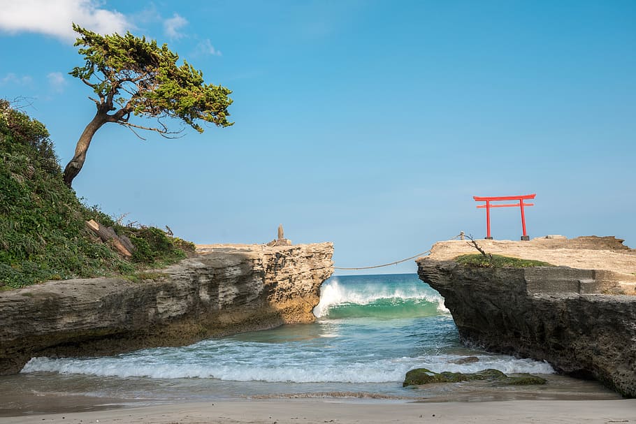 torii arch on top of cliff under clear skies during daytime, beach