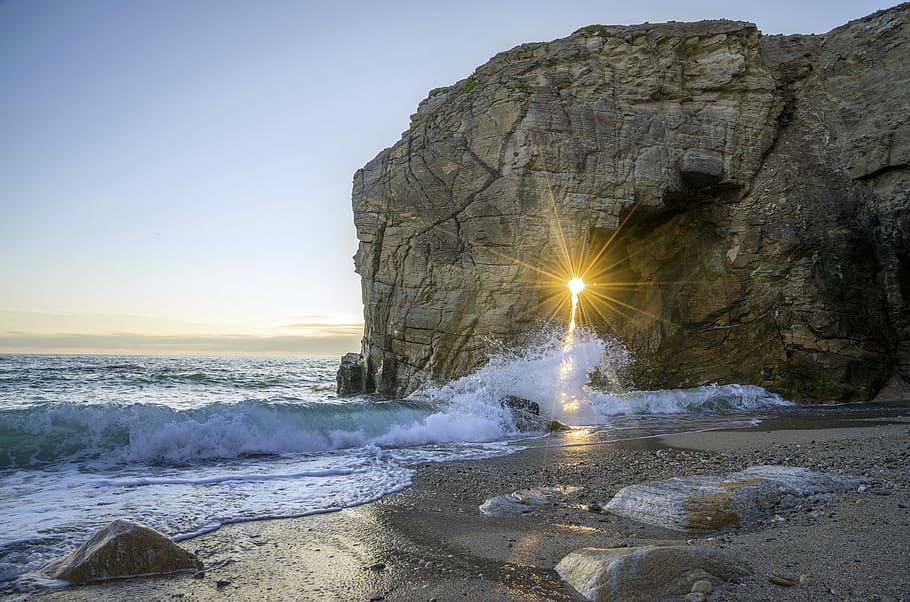 sea wave splashing in seashore beside mountain, brown rock formation beside sea during daytime HD wallpaper