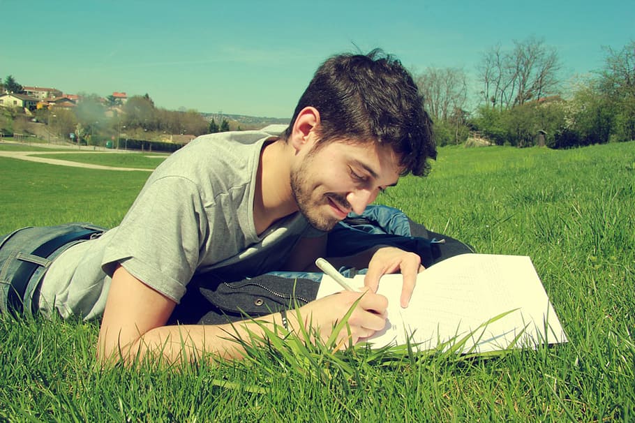 male laying on grass holding pen, man in gray, shirt, field HD wallpaper