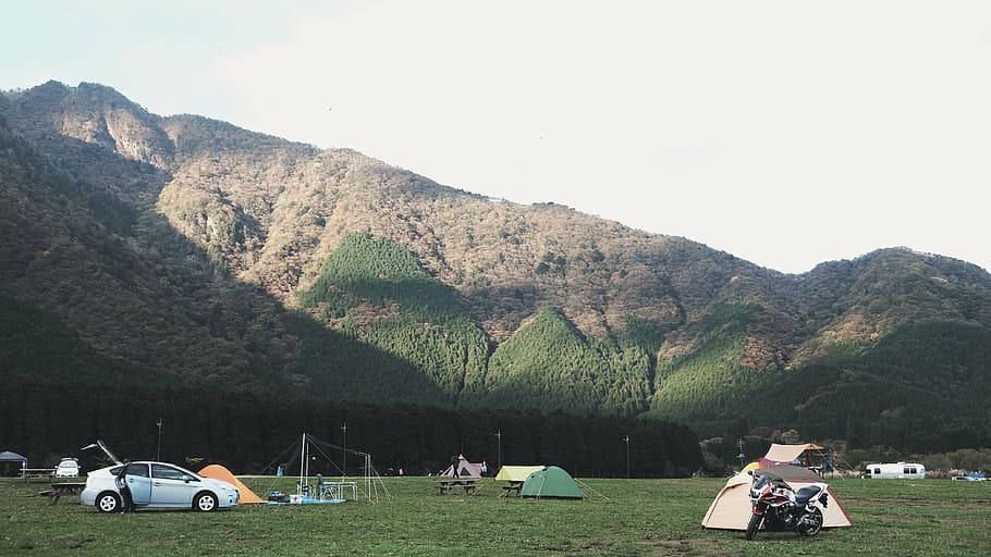 white car on green field near camping tents and mountain during daytime HD wallpaper