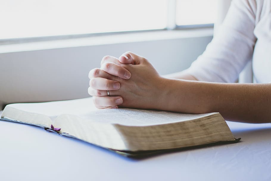 person sitting with both hand on book top, prayer, bible, christian