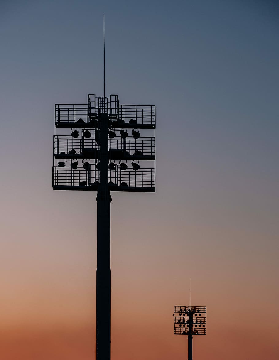 silhouette of two spot light tower, two metal towers with lights during golden hour HD wallpaper