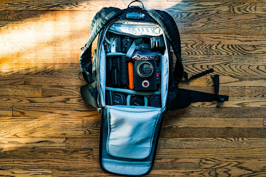 flat-lay photography of DSLR camera in backpack on wood parquet floor, gray trail camera bag on brown wooden panel HD wallpaper