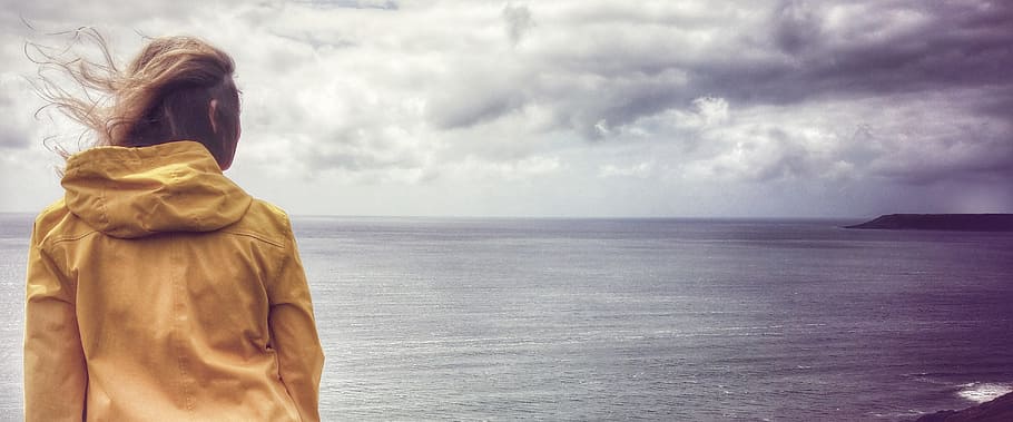 woman wearing hooded jacket facing sea, breeze, yellow, clouds HD wallpaper