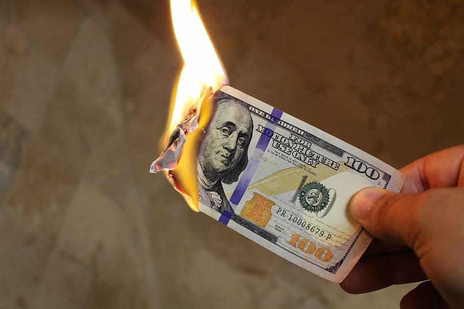 person holding 100 U.S. Dollar banknote, burning money, dollars