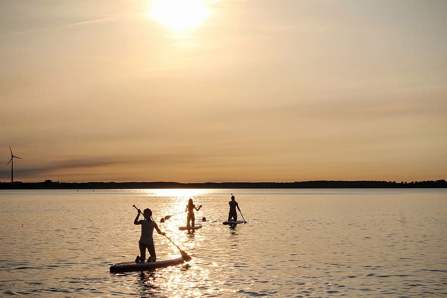 three people riding paddle board under golden hour, stand up paddle