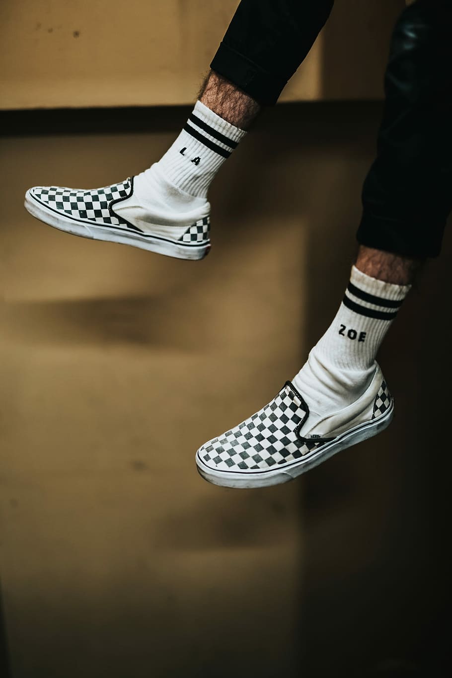 person wearing white-and-black checked slip-on shoes, person wearing pair of white-and-black Vans low-top sneakers