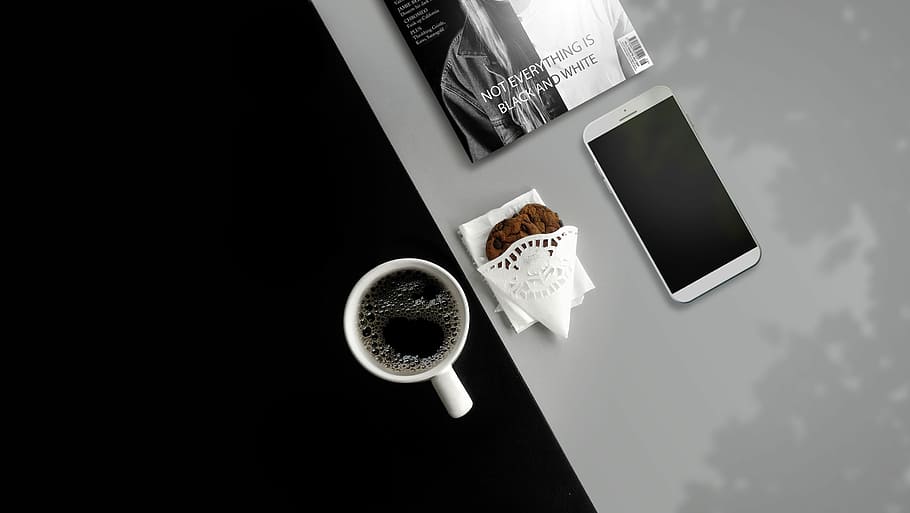 white ceramic mug filled with black liquid, silver smartphone, cup of coffee, and chocolate chip