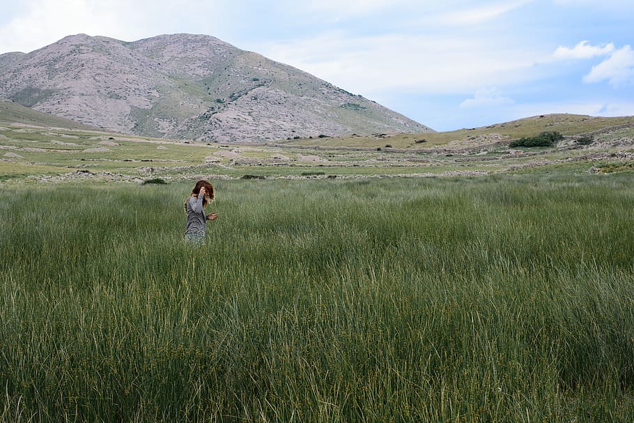 person on green grass field, person wearing gray top walking on green grassland near mountain range HD wallpaper