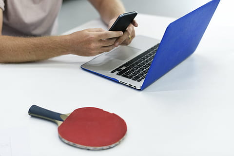 person holding smartphone beside MacBook and table tennis paddle HD wallpaper